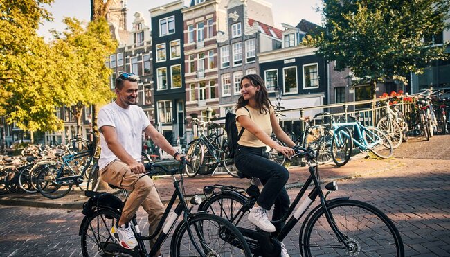 Intrepid traveller couple cycling through the streets of Amsterdam, Netherlands