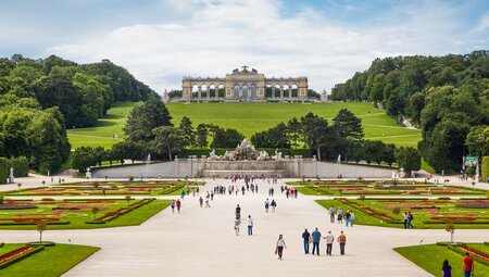 Travellers and locals wander the curated gardens of Schonbrunn Palace in Vienna Austria