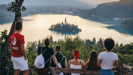 Group of travellers and leader look out over reflective Lake Bled from Ostrica mountain in Slovenia