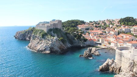 A ultra-wide shot of Fort Lovrijenac, a square fortress, on a rocky coastal cliff on a sunny day