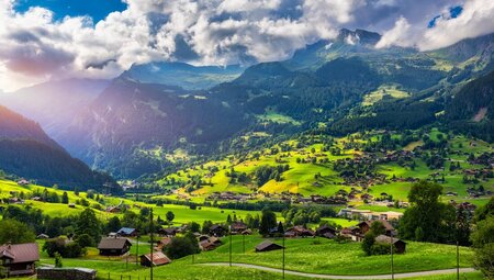 Sun sprays across Grindelwald village sprawling across bright green valley in the mountains of the Swiss Alps