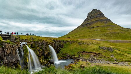 Group of travellers stand above Kirkjufelsfoss waterfall on the Snæfellsnes Penninsula