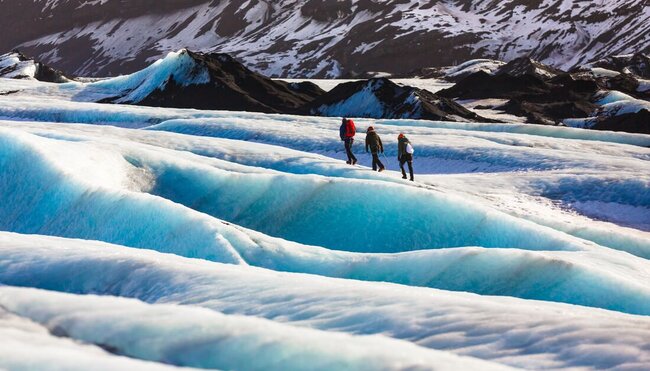 Travellers glacier hiking in Solheimajokull, Iceland with snow covered mountains in the background