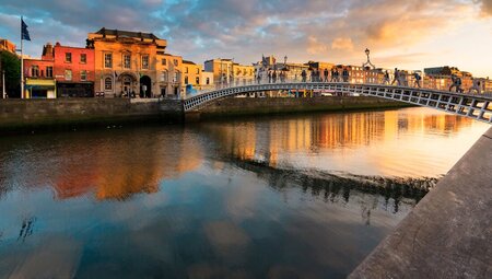 People walking over water on the Hapenny Bridge at a colourful sunset in Dublin, Ireland