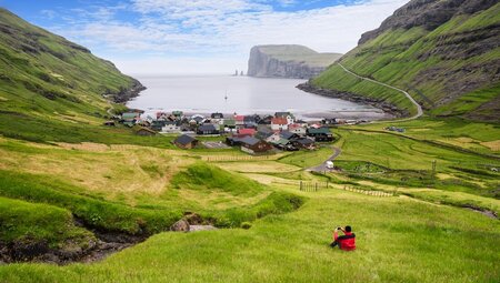 Intrepid traveller perched on the hills above Gjogv viewing to Risin og Kellingen in theh Faroe Islands