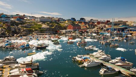 Ilulissat harbor with a number of docked boats and small icebergs in the harbor, buildings and town beyond