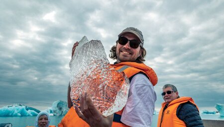 Intrepid traveller smiles, holding a huge shard of fesh ice from the Jokulsarlon Glacier Lagoon in their hands