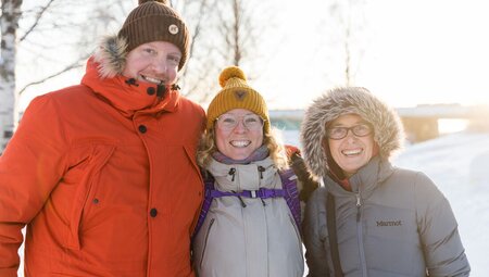 Leader and travellers in heavy winter coats smile in the snowy city of Rovaniemi