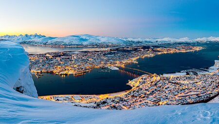 High vantage look out over city of Tromso in winter glowing building lights with blanket of snow on the coast