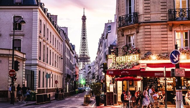 Brightly lit cafes on the streets of Paris in the evening light, Eiffel Tower visible in background
