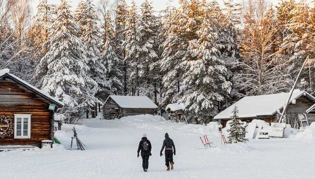 Two travellers walk through thick snow to get to cabin in Finland