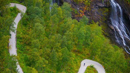 Intrepid travellers cycles the winding Rallarvegen road Myrdal to Flam with waterfalls nearby in Norway