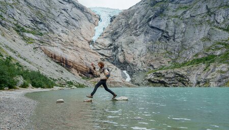 Intrepid traveller carefree rock hopping before Briksdalen Glacier, Jostedalsbreen National Park in Norway