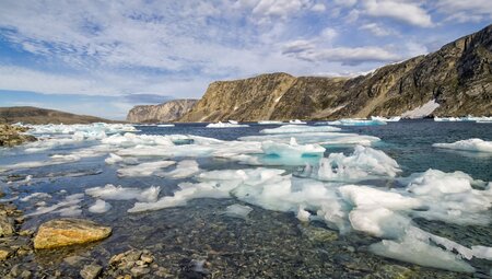 Wide landscape view of Cape Mercy Glacial Fjord with small icerbegs in the bay and rocky mountains beyond