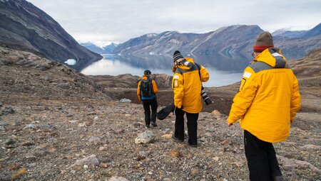 Travellers in yellow Quark coats hiking in the majestic landscape of Blomsterbugten (Flower Bay)