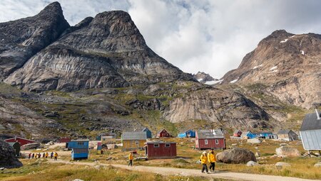 Travellers exploring the town of Aappilattoq in southwestern Greenland with looming mountains