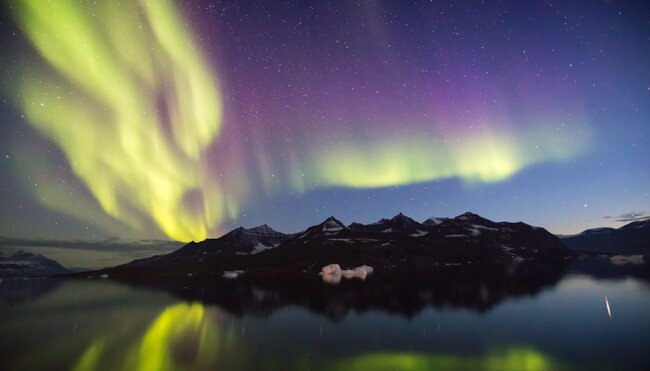 Yellow green and magenta waves of iridescent northern lights undulate over the Greenland landscape at twilight