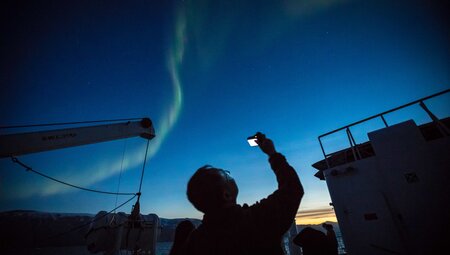 Traveller takes a photo up looking at the Aurora Borealis Northern Lights over east Greenland