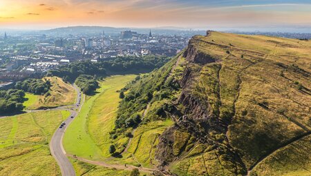 View of Edinburgh from Arthur's Seat top, with travellers climbing Salisbury Crags in the foreground