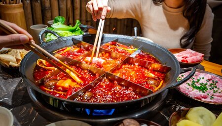 Travellers reach into and dine on a classic Chongqing hotpot with a 9 part divider in Hunan
