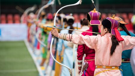 Naadam festival women's archery, women in traditional Mongolian dress shooting arrows with Mongol bow and arrow