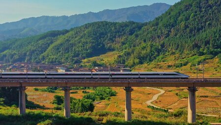 Bullet train on high rail line passing through the mountain backed agricultural landscape of Yunnan Province China