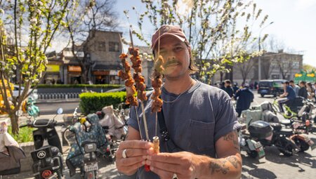 Intrepid traveller holds up Beijing lamb skewers, streetfood bought on a real food adventure tour in China