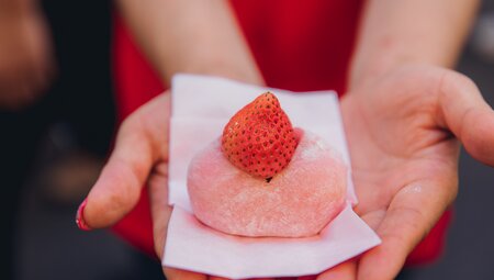 A frosted gelatinous ball dessert topped with a strawberry held in traveller's hands in Tokyo food markets