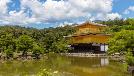 Kinkaku-ji Temple Golden Pavilion at the edge of a curated pond on a sunny day with clouds above