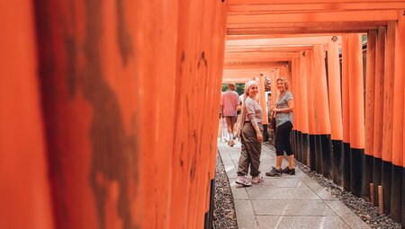 Travellers look back at viewer from the endless rows of Fushimi Inari orange shrine gates near Kyoto Japan