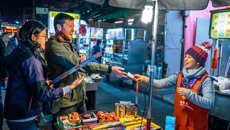 Two travellers talk happily with shop owner as they buy gifts in Taipei night markets