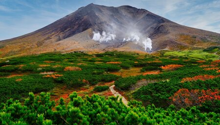 Autumn reds and oranges mix with spring greens in the foliage leading up to the bare face of Mt Asahi in Hokkaido
