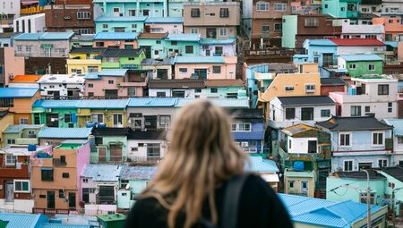 Traveller looks out at colourful facades of pastel houses at an overlook in Gamcheon Culture Village