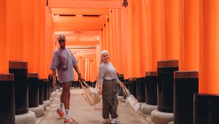 Intrepid travellers having fun while exploring Fushimi Inari shrine walking through the orange gates near Kyoto