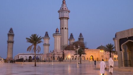 Towering spires of the Great Mosque of Touba at dawn in northern Senegal with locals in foreground