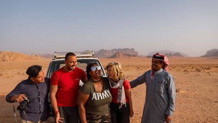 Travellers laugh with leader and local guide waiting for sunset in Wadi Rum on a 4x4 vehicle