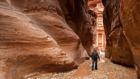 Traveller walks between slim walls of gorge with view of petra at the end