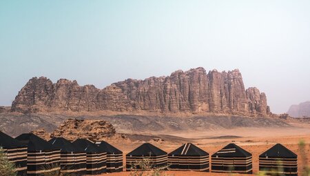 Wide view of black tents at Bedouin camp with mountain range in the background, Jordan