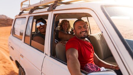 Intrepid leader and travellers smile excitedly at the camera on a 4x4 ride through Wadi Rum