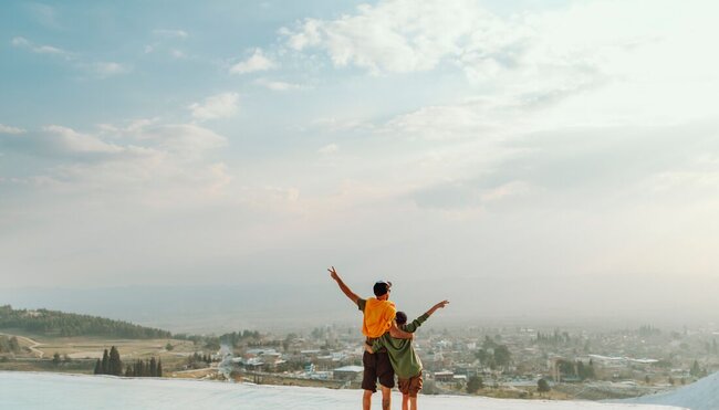 Intrepid traveller father and son throw up their hands in joy on the edge of the TUrkish landscape in Pamukkale pools