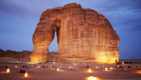 Travellers seated in the sand enjoying twilight at Jabal Alfil, elephant rock, Al Ula, Saudi Arabia