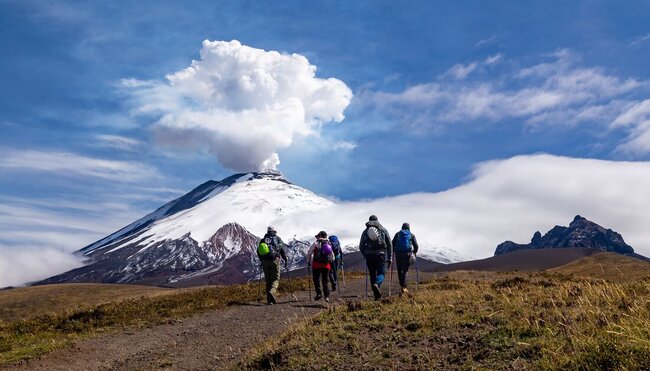 Cotopaxi volcano eruption with travellers hiking in foreground, Cotopaxi NP, Ecuador