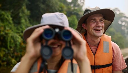 Intrepid traveller looks through binoculars for wildlife on the Amazon river in Peru