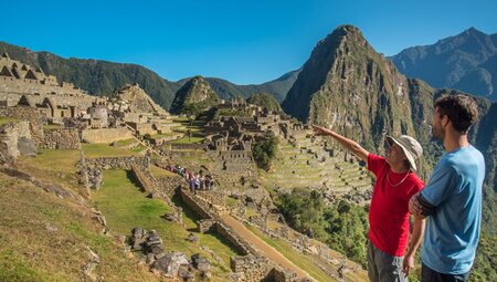 Guide points to ruins of Machu Picchu in the distance while talking to traveller in Peru