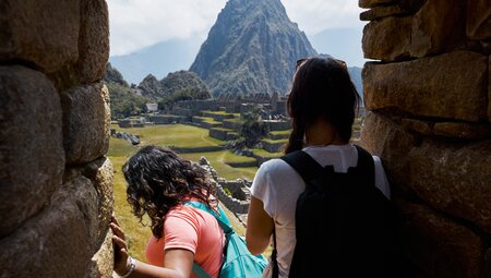 Intrepid travellers at Machu Picchu emerges from tunnel building looking at Huayna Picchu in Peru
