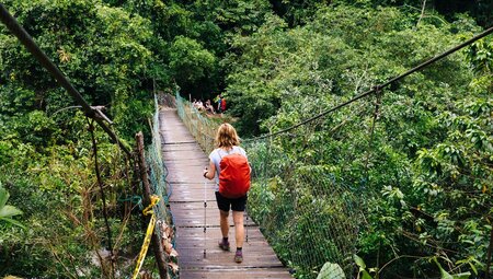 Traveller with red backpack crossing a bridged river on the way to Ciudad Perdida or the Lost City