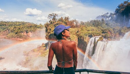 Intrepid traveller 18 to 35 marvelling at the surroundings of Iguazu falls as a rainbow arches in front
