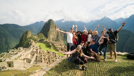 Group of excited travellers in activewear pose at the Machu Picchu lookout in Peru