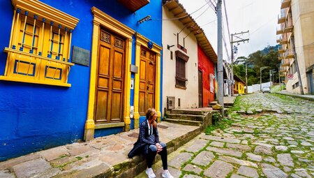 Travelling sitting on the street paved with cobblestone, surrounded by bright colourful buildings in Bogota, Colombia