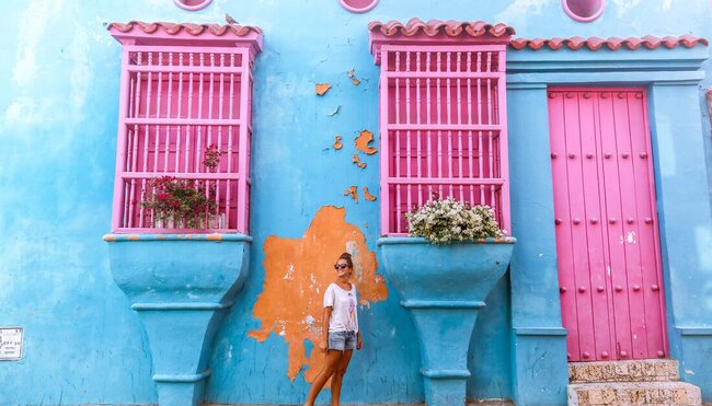 Traveller smiling in front of bright blue and pink building in Cartagena, Colombia